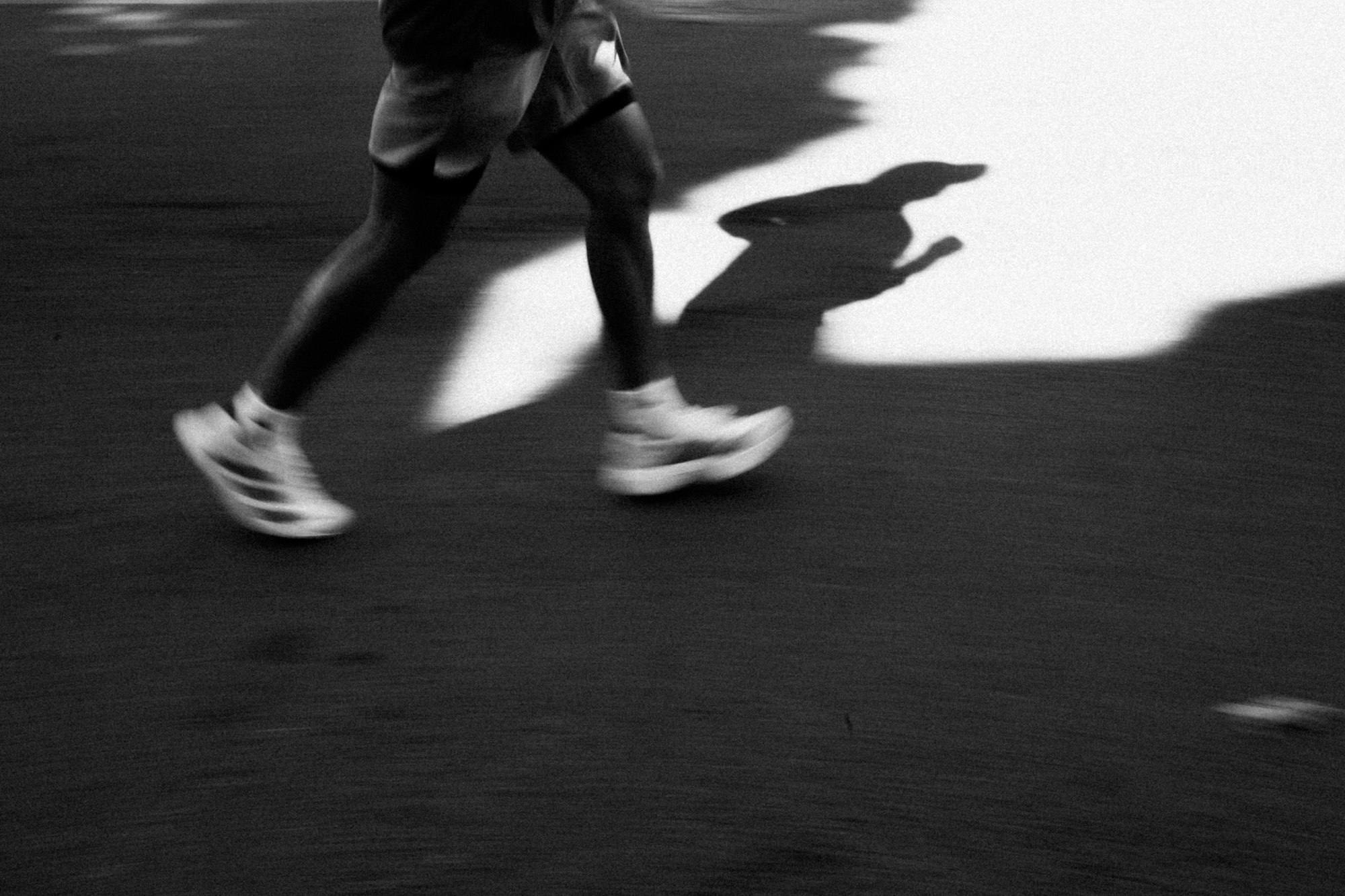 A runner's legs in motion with a long shadow